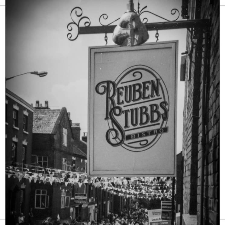 The Reuben Stubbs Bistro hanging sign in a black-and-white street photograph